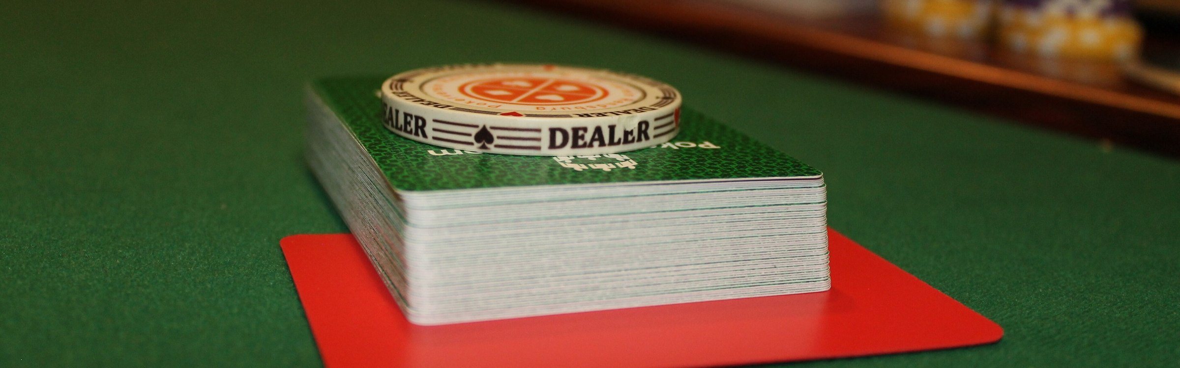 Baralho de cartas e botão de dealer sobre a mesa de feltro verde